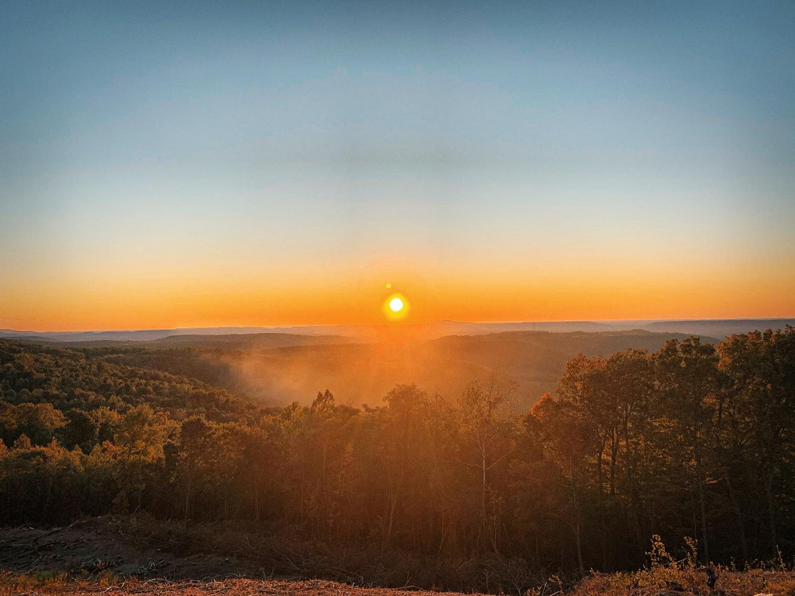 Sun rising over a distant wooded ridgeline